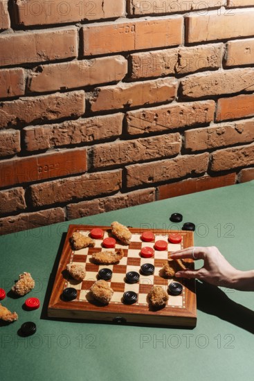 A creative take on checkers using chicken nuggets as game pieces on a board, set against a rustic brick wall. A hand engaged in play, bringing a fun twist to dining