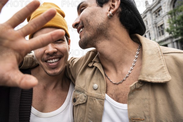 A happy gay couple enjoys a day out, displaying affection and a carefree attitude. The focus is on their joyful expressions and the urban backdrop adds character to their moment