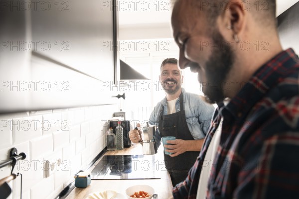 Two gay men enjoy preparing a meal together in a modern kitchen. One holds a coffee pot while the other focuses on chopping vegetables, capturing a moment of joy and togetherness
