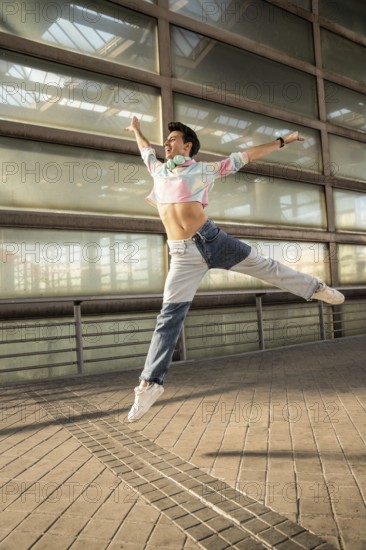 A young man in a colorful shirt and jeans joyfully leaps against a modern urban backdrop. He wears headphones, exuding energy and passion in his dance move
