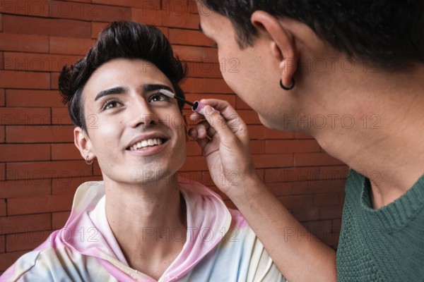 A loving couple, with one applying makeup to the other's lashes. Their joyful expressions and soft interaction highlight love while embracing individuality and creativity within the relationship