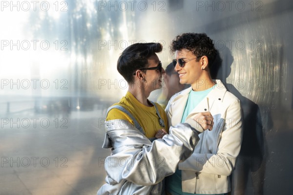 A joyful gay couple, wearing casual clothes and sunglasses, share a tender moment while smiling at each other. The scene is warm and vibrant, capturing love and connection