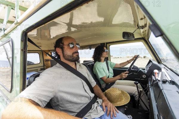 A blind man relaxes in a motorhome while a woman drives. The scenic coastal setting enhances the sense of freedom and adventure in this unique and inclusive travel experience