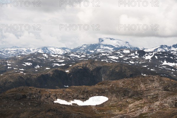 A stunning view of Norway's rugged mountains, dotted with patches of snow The dramatic clouds and expansive terrain highlight the untouched beauty of this Nordic wilderness