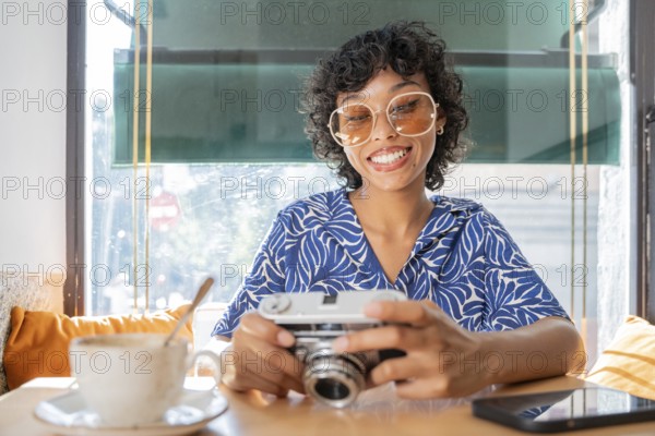 A cheerful woman at a cafe, holding a vintage camera, with a cup of coffee in the foreground. Sunlight filters through a window, creating a warm, inviting ambiance