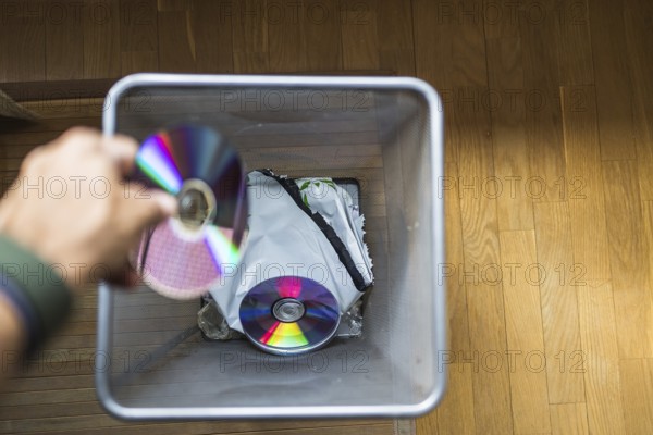 A hand discards CDs into a trash bin, symbolizing the shift from physical media to digital formats. The image highlights technology evolution and the decline of traditional storage