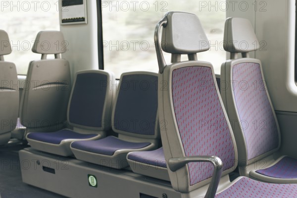 A row of empty train seats with purple upholstery and patterned design by a window. The setting captures a calm, quiet transport atmosphere, highlighting public transit design