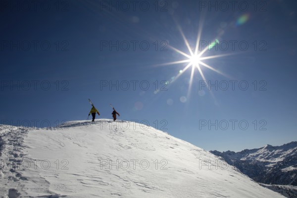 Two skiers hike up a snow-covered mountain under a bright sun, ready for an exhilarating freeride descent The pristine blue sky enhances the scenic alpine backdrop