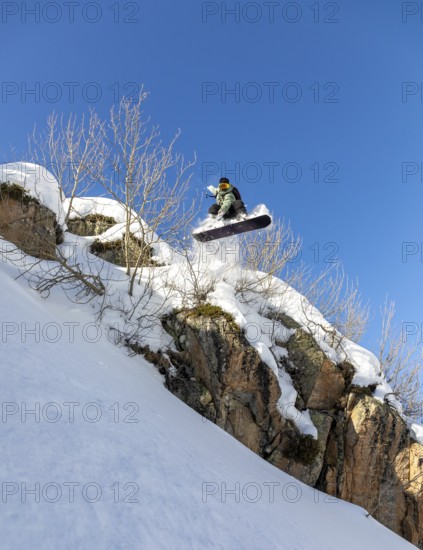 A daring snowboarder leaps off a snowy cliff, showcasing thrilling winter sports skills against a clear blue sky. The scene captures the excitement and adrenaline of mountain adventures