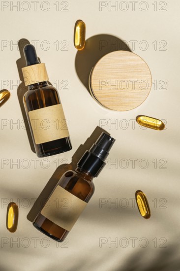 Top view of an amber glass cosmetic bottles with blank labels surrounded by soft shadows and golden capsules on a beige background, creating a luxurious skincare presentation
