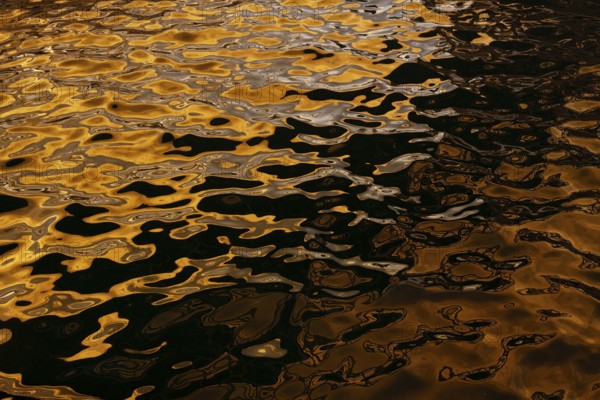 Artistic close-up of shimmering water reflecting golden hues under sunlight at Playa Blanca Port, Lanzarote, capturing the mesmerizing patterns formed