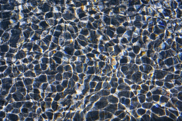 Sunlight dances on the rippling waters of Playa Blanca Port, Lanzarote, creating a mesmerizing pattern of light and shadow