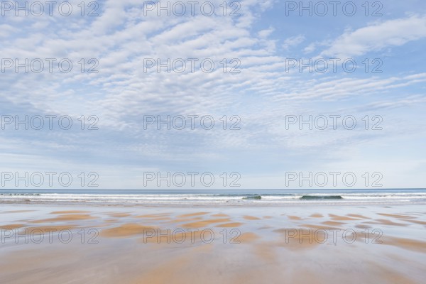A tranquil beach scene featuring an expansive view of gentle waves under a sky filled with soft clouds, highlighting the natural beauty of an undisturbed shoreline