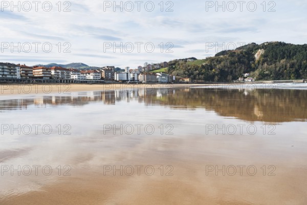 A serene image capturing a coastal town's reflection on a calm bay under a clear sky, showcasing nature's beauty and the town's architecture