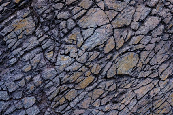 Detailed view of a jagged rock surface with interlocked gray and rust-colored stones in Mujeres Beach, Lanzarote. Highlighting intricate natural patterns and rough texture