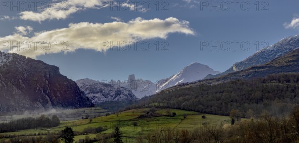 Stunning panoramic view of the mountains, showing snow-capped peaks and lush green valleys under a clear blue sky with clouds