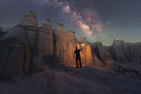 A lone figure illuminates the magnificent sandstone formations of Goblin Valley State Park, Utah, under a breathtaking starry sky, highlighting the Milky Way