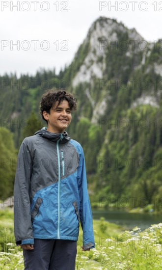 A smiling individual stands against the picturesque backdrop of Lac de Taney, Switzerland, surrounded by lush greenery and majestic mountains, exuding joy and adventure