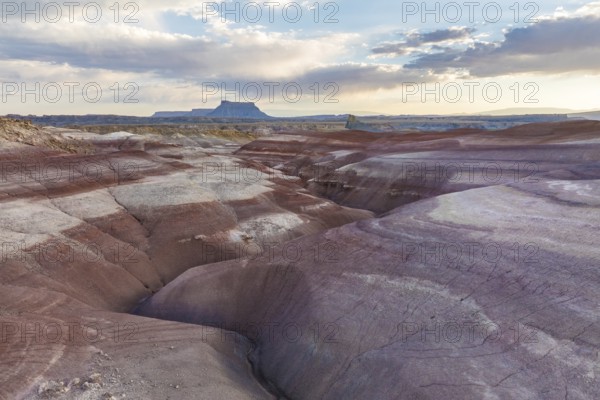 Stunning aerial shot capturing the multi-colored, layered bentonite hills in a desert landscape under a soft sunset sky, showcasing the natural beauty and geological uniqueness of Utah, USA