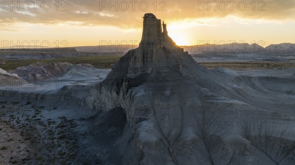 A breathtaking view of the sun setting behind a towering rock formation in Utah, casting a warm glow over the weathered landscape and intricate geological textures