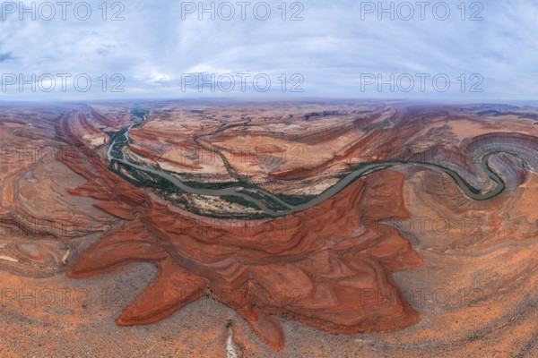 A breathtaking aerial view of a desert landscape. A winding river cuts through red rock San Juan canyons under a vast, cloudy sky, showcasing nature beauty and grandeur of Utah, USA