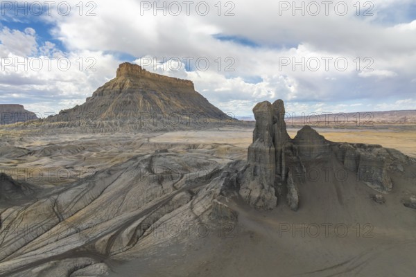 A breathtaking landscape featuring a towering desert mesa and striking rock formations under a vivid blue sky with scattered clouds in Hanskville, Utah. The scene captures nature grandeur of USA