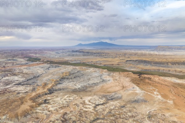 A stunning aerial drone view capturing the vast, rugged landscape of Hanksville, Utah, highlighting the unique geological features and vast expanses under a hazy sky