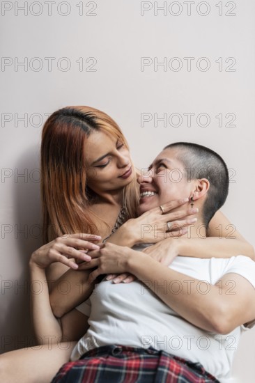 A lesbian couple enjoys a tender embrace, sharing smiles and happiness. Their affectionate connection is highlighted by their shared laughter and relaxed pose