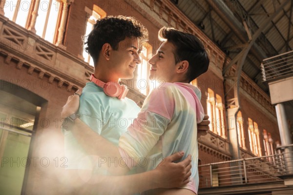 A joyful gay couple embraces lovingly against an urban backdrop, bathed in warm sunlight. The intimate moment captures the essence of romance and affection in a vibrant setting