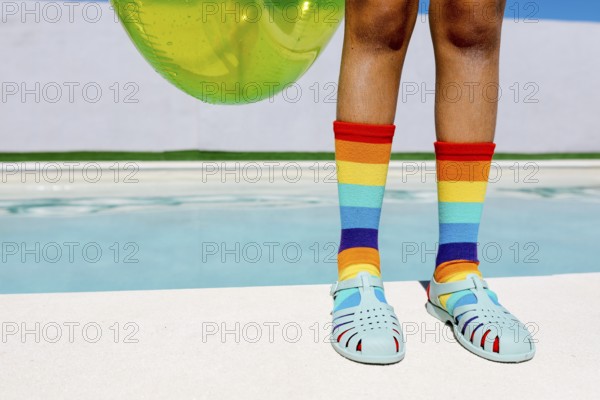 Vibrant rainbow socks and turquoise sandals by a pool, capturing summer's essence. The bright colors and inflatable tube evoke fun, warmth, and relaxation