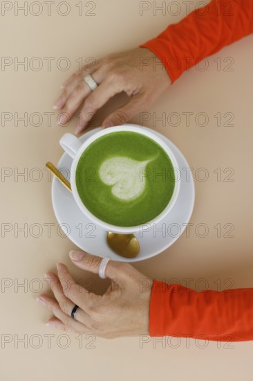 A woman enjoys a matcha latte in a Warsaw cafe Her vibrant orange clothing and trendy rings add flair to the serene setting, showcasing contemporary lifestyle