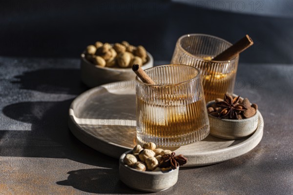 Spiced cognac-based cocktails garnished with cinnamon sticks and star anise, accompanied by almonds, peanuts, and mixed nuts, presented on stylish ceramic tableware