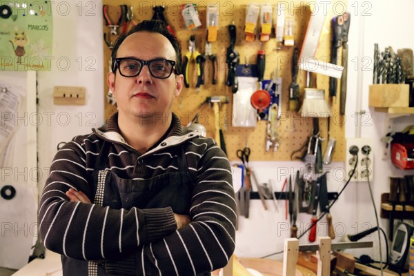 A luthier stands confidently in a bass guitar workshop, surrounded by tools and equipment. The workspace reflects creativity, craftsmanship, and dedication to musical artistry