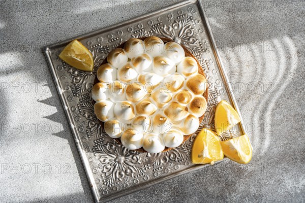 Top view of a homemade lemon cake on a decorative tray surrounded by lemon wedges. The dessert is beautifully lit by natural sunlight, casting intricate shadows