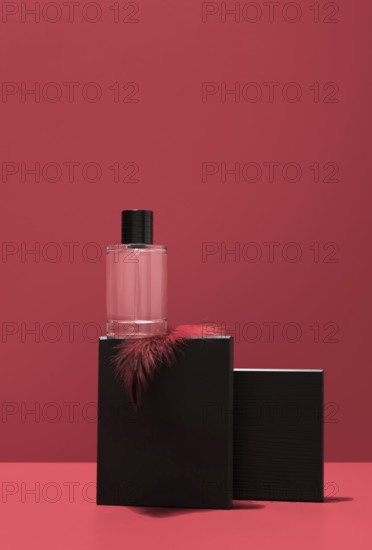 A sleek perfume bottle rests on a black stone stand, elegantly highlighted against a vibrant red background, conveying a sense of luxury and sophistication