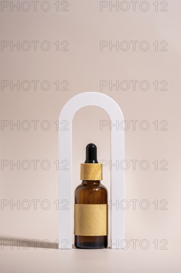An amber glass dropper bottle with a wooden cap and blank label is elegantly placed in a white arch frame against a beige background, highlighting minimalist design