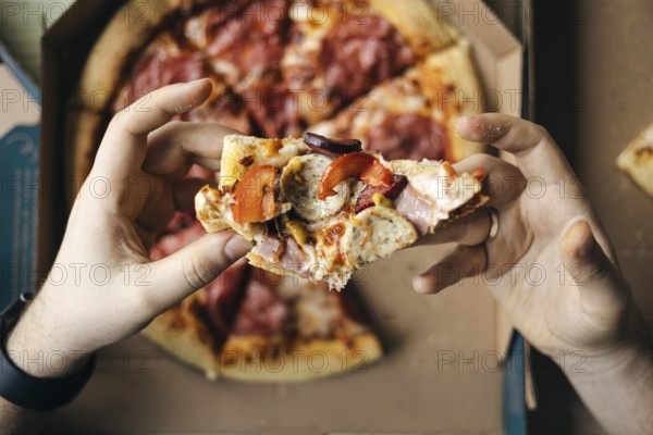 From above cropped unrecognizable close-up of a person's hands holding a piece of pepperoni and sausage pizza, showing details of the toppings and the crust