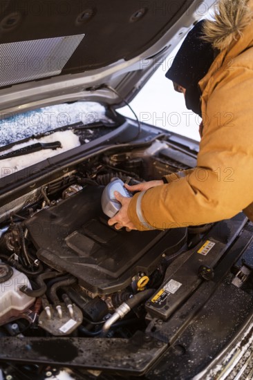 A person in winter clothing checks car fluids in snowy Swedish Lapland. Hood open, engine exposed, essential winter auto care. Cozy and practical scene