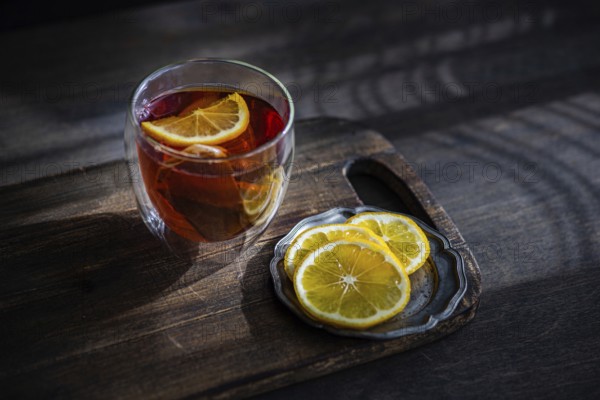 A cozy setting features a glass of rich, aromatic English tea with vibrant lemon slices, placed on a rustic wooden table, highlighting a moment of relaxation