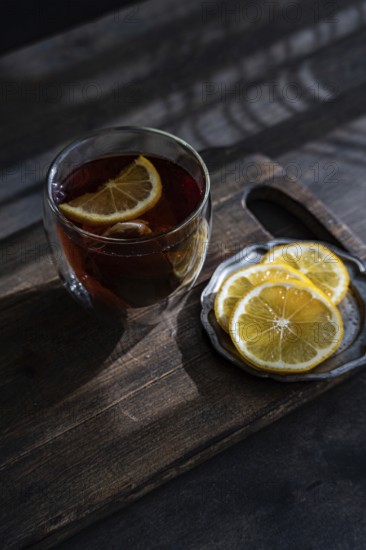 A clear glass filled with amber-colored tea accompanied by fresh lemon slices, set against a rustic wooden backdrop, evokes a cozy, traditional English tea time