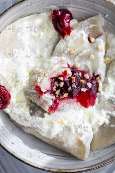 Traditional Ukrainian varenyky filled with cherry, topped with sour cream and sprinkled with chopped nuts. A delightful taste of Eastern European cuisine