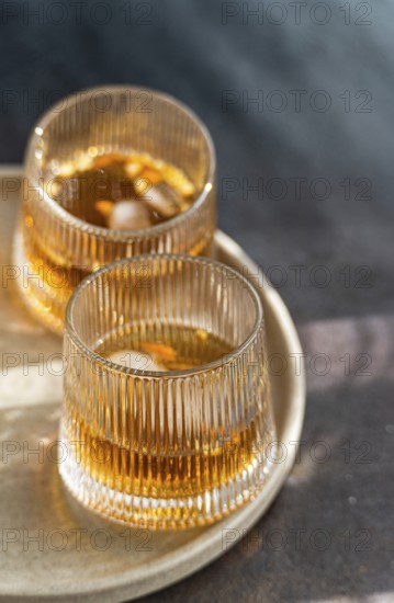 Two glasses of spiced cognac cocktail with cinnamon and star anise, accompanied by assorted nuts, elegantly presented on a textured tray