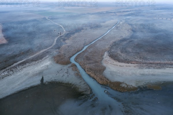 Aerial view of a lagoon in Toledo, Spain, with visible common cranes in their natural habitat. The tranquil landscape showcases flowing water, wetlands, and diverse wildlife in a peaceful ecosystem