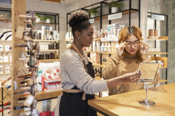 A worker in a cosmetics store helps a customer choose products. They stand by a counter filled with beauty supplies, surrounded by shelves displaying various items