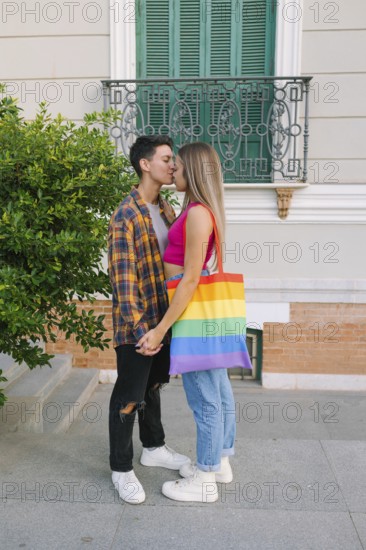 A happy lesbian couple shares a tender moment outdoors, celebrating their love and pride. One partner carries a Pride flag bag, symbolizing LGBTQIA+ pride, inclusivity, love, and diversity