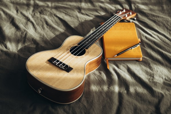 A ukulele rests on a bed beside a yellow notebook and pen, bathed in soft natural light This cozy setup evokes creativity and relaxation, ideal for music lovers