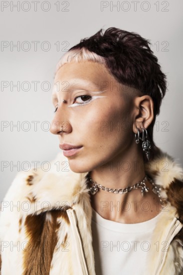 Wide angle close-up of a woman with a bold hairstyle, glamorous nose and ear piercings, striking white eyeliner, and a faux fur jacket, creating a modern fashion statement