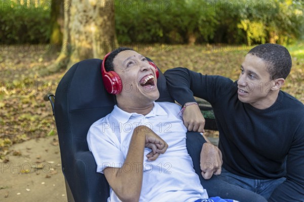 Spanish Cameroonian siblings share a joyful outdoor moment at a park. One sibling, wearing headphones, has cerebral palsy, highlighting the family's Mixed-race bond