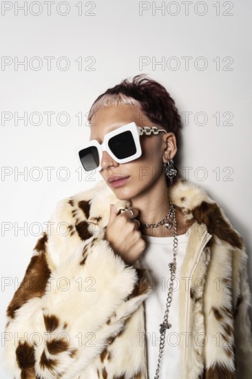 Fashion-forward woman wearing a faux fur coat and oversized white sunglasses, showcasing trendy jewelry. The chic look highlights contemporary style and luxury