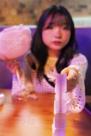 An Asian Gen Z girl delights in the arcade atmosphere, holding cotton candy while playing a game The colorful lights and playful vibe capture youthful fun and joy
